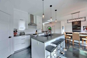 A modern kitchen with a central island, bar stools, and pendant lighting. - Condos Monts-Valin- 213, rue du Massif (Valinouët) (Saint-David-de-Falardeau)