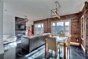 A modern kitchen with a central island, wooden walls, and large windows offering a view. - Condos Monts-Valin- 213, rue du Massif (Valinouët) (Saint-David-de-Falardeau)