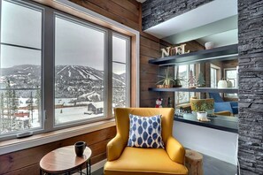A cozy room with a large window offering a scenic mountain view, a comfortable yellow armchair, and a wooden table with a cup. - Condos Monts-Valin- 165, rue du Massif (Valinouët) (Le Fjord-du-Saguenay Regional County Municipality)