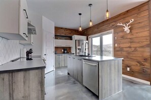 A modern kitchen with a central island, stainless steel appliances, and pendant lighting. - Condos Monts-Valin- 165, rue du Massif (Valinouët) (Le Fjord-du-Saguenay Regional County Municipality)