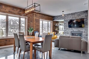 A modern living room with a stone wall, a fireplace, and a TV mounted on the wall. - Condos Monts-Valin- 165, rue du Massif (Valinouët) (Le Fjord-du-Saguenay Regional County Municipality)