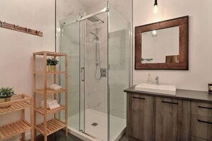 A modern bathroom with a glass-enclosed shower, wooden shelves, a sink with a mirror, and a wooden cabinet. - Condos Monts-Valin- 165, rue du Massif (Valinouët) (Le Fjord-du-Saguenay Regional County Municipality)