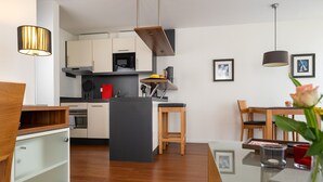 A modern kitchen with wooden cabinets, a central island, and a dining area with a glass table. - 5-Star Comfort Holiday Home Jümmers: 'Trientje', Prime Location by Wadden Sea National Park (Wangerland-Horumersiel)