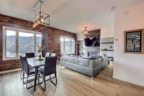 A modern living room with a grey sofa, dining table with chairs, a fireplace, and a TV mounted on the wall. - Condos Monts-Valin -151, rue du Massif (Valinouët) (Saint-David-de-Falardeau)