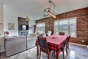 A modern kitchen with a stone backsplash, wooden walls, a dining area with a checkered tablecloth, and a large window offering a view of the outdoors. - Condos Monts-Valin -149, rue du Massif (Valinouët) (Saint-David-de-Falardeau)