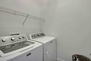 A laundry room with a front-loading washer and dryer, a metal drying rack, and a basket. - Condos Monts-Valin -149, rue du Massif (Valinouët) (Saint-David-de-Falardeau)