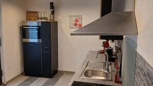 Cozinha compacta com forno embutido, pia de aço inoxidável e bancada pequena.