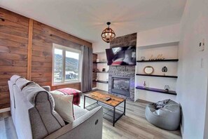 A modern living room with a fireplace, a sofa, a coffee table, and a television mounted on the wall. - Condos Monts-Valin -161, rue du Massif (Valinouët) (Saint-David-de-Falardeau)