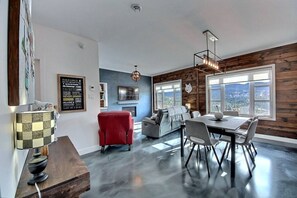 A modern living room with a dining area, wooden walls, and large windows offering a view. - Condos Monts-Valin- 211, rue du Massif (Valinouët) (Le Fjord-du-Saguenay Regional County Municipality)