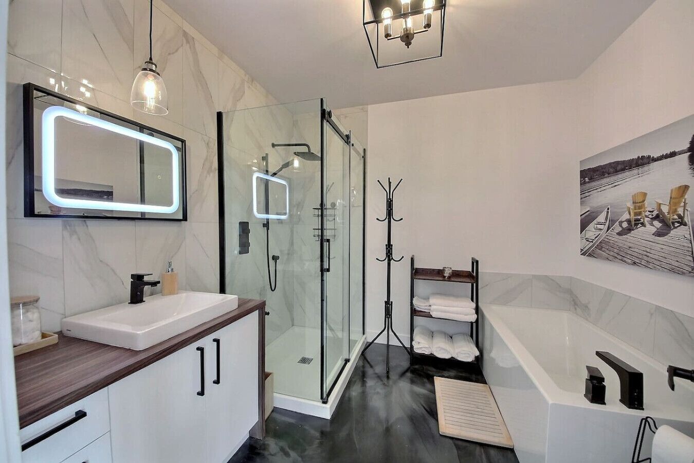 A modern bathroom with a glass shower enclosure, a large mirror with LED lighting, and a bathtub with a towel rack.