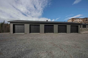 A building with six garage doors, a gravel driveway, and a clear sky. - Condos Monts-Valin- 205, rue du Massif (Valinouët) (Saint-David-de-Falardeau)