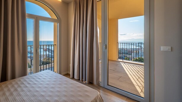 A bedroom with a large window and sliding glass door to a balcony with a city view. - 13 -Villa Pignone Three-room Superior apartment with balcony (Genova)