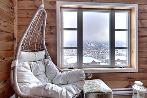 Ein gemütliches Zimmer mit Hängesessel, Fenster mit Blick auf Schnee und kleiner Tisch mit Glas.