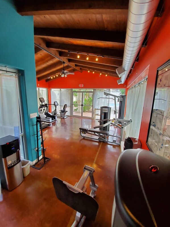 A gym with various exercise equipment, a water dispenser, and large windows allowing natural light.