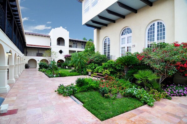 A courtyard with a paved walkway, surrounded by lush greenery and flowering plants.