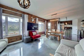 A modern living room with a red sofa, a flat-screen TV, and a dining area with a wooden table. - Condos Monts-Valin -159, rue du Massif (Valinouët) (Saint-David-de-Falardeau)