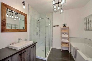 A modern bathroom with a glass shower enclosure, a vanity with a mirror, and a built-in shelf with towels. - Condos Monts-Valin -157, rue du Massif (Valinouët) (Saint-David-de-Falardeau)