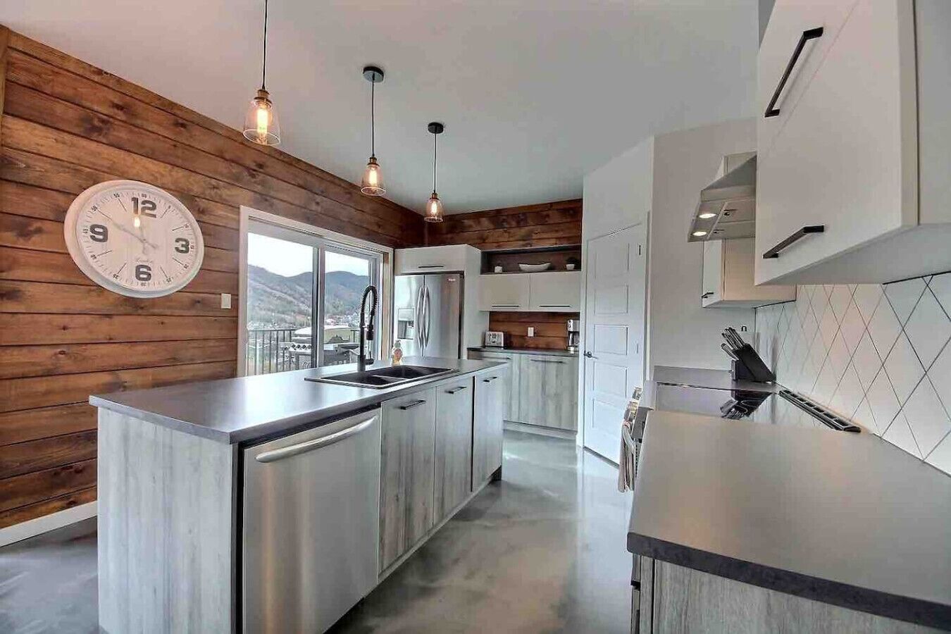 A modern kitchen with stainless steel appliances, wooden wall paneling, and pendant lighting.
