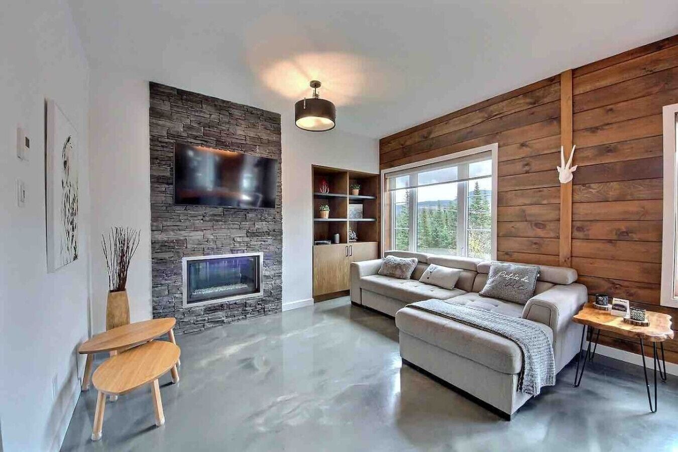 A modern living room with a stone fireplace, a large window, and a wooden wall.