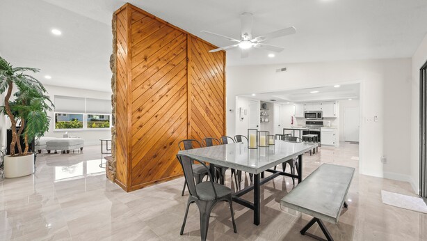 A modern dining area with a large table, chairs, and a wooden accent wall. - 90+ Day Furnished Retreat! Heated Pool, Spa, Game Room, and 4 King Beds! (Merritt Island)