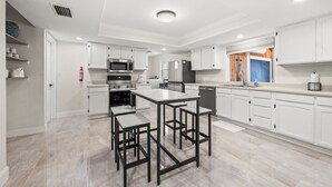 A modern kitchen with white cabinetry, stainless steel appliances, and a central island with bar stools. - 90+ Day Furnished Retreat! Heated Pool, Spa, Game Room, and 4 King Beds! (Merritt Island)