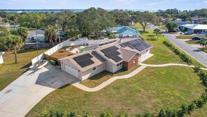 A residential property with a large house featuring multiple solar panels, a garage, and a well-maintained lawn. - 90+ Day Furnished Retreat! Heated Pool, Spa, Game Room, and 4 King Beds! (Merritt Island)