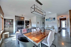 A modern living room with a wooden dining table, grey sofas, and a fireplace. - Condos Monts-Valin -163, rue du Massif (Valinouët) (Saint-David-de-Falardeau)