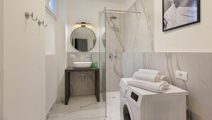 Un bagno moderno con lavabo in marmo, cabina doccia in vetro e lavatrice integrata.