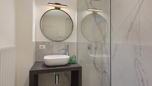 Un bagno moderno con uno specchio rotondo, un lavandino bianco e una cabina doccia in vetro.