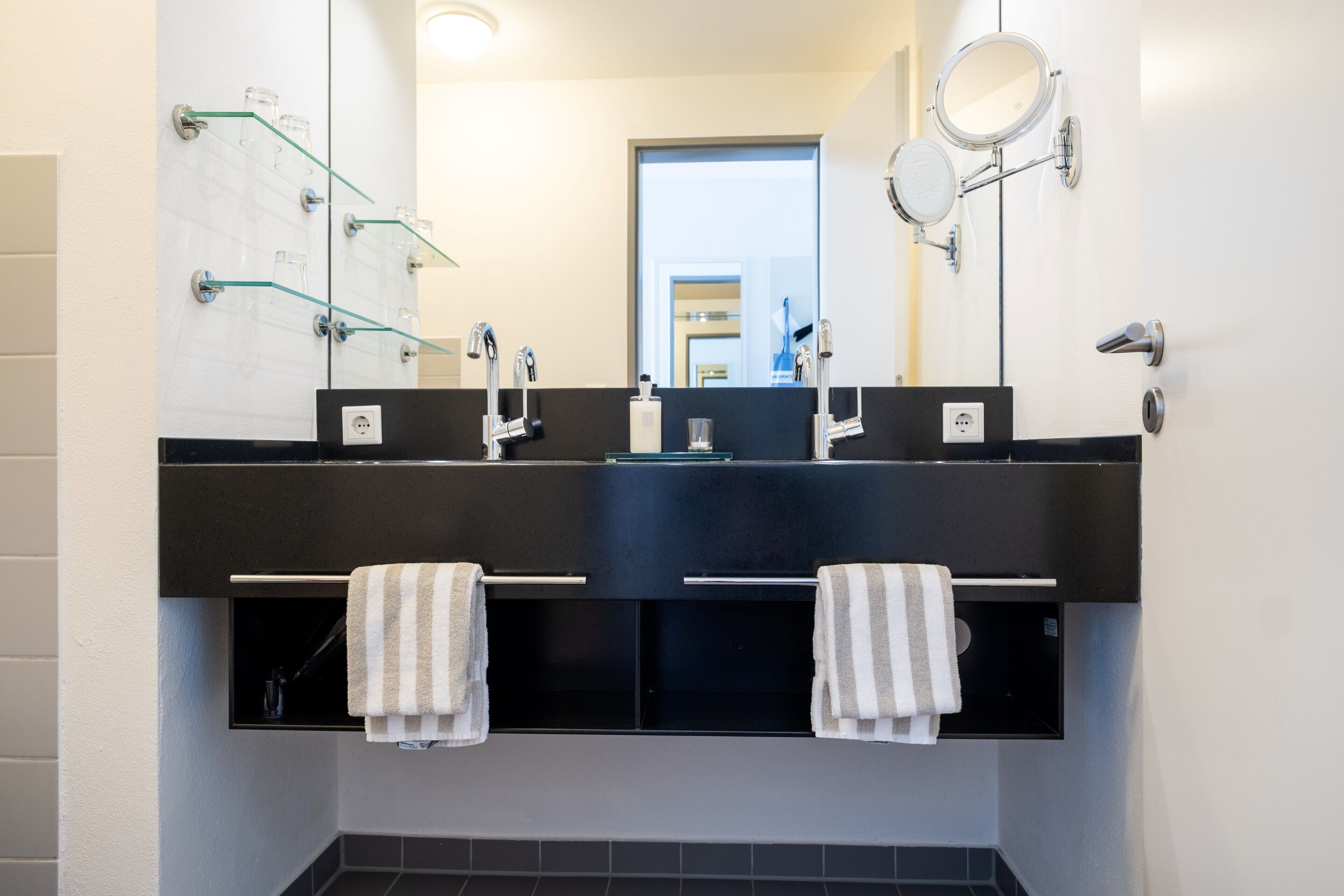 Een moderne badkamer met een zwart wastafel, twee spiegels en glazen handdoekhouders.