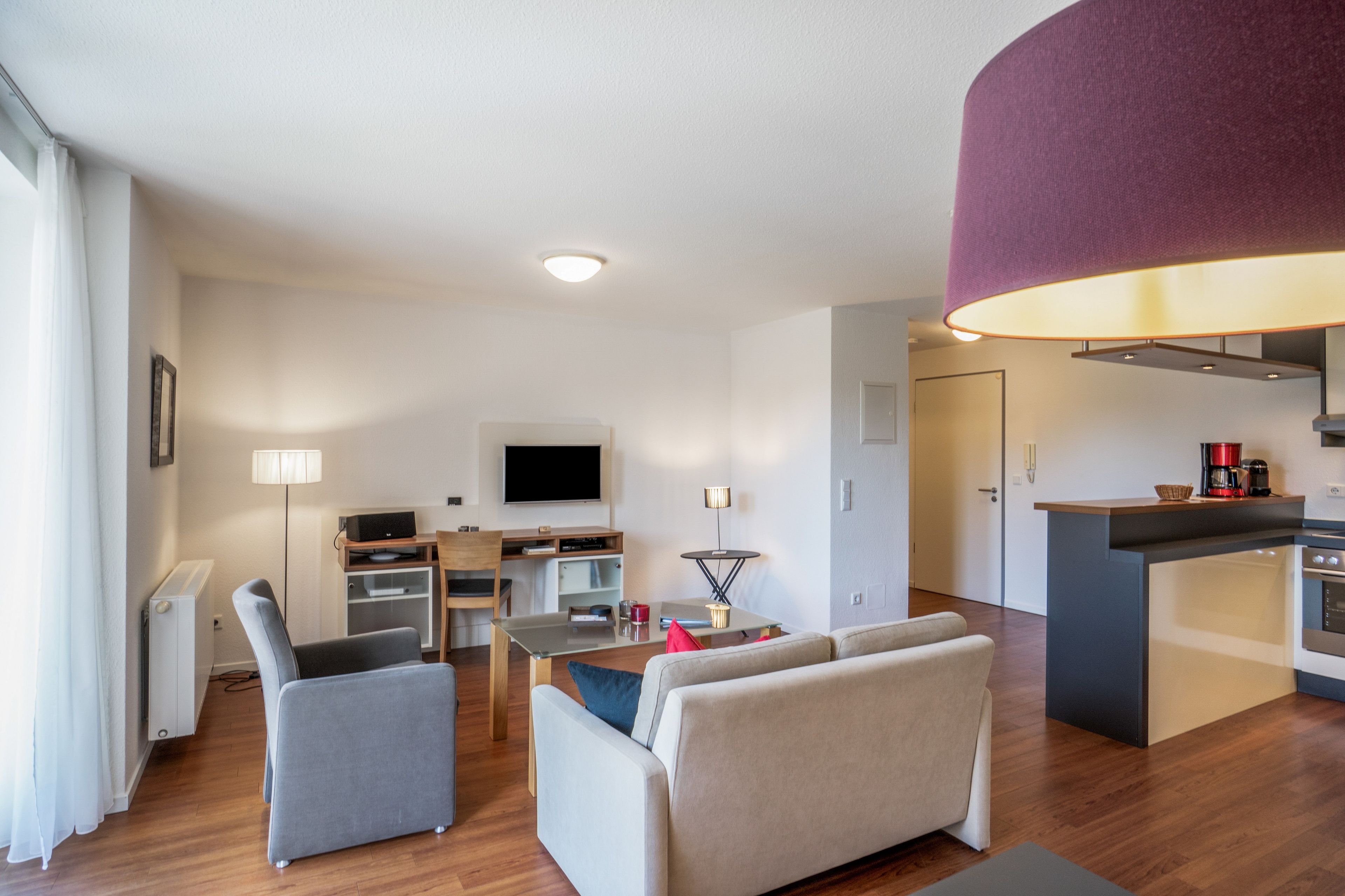 Ein modernes Wohnzimmer mit Flachbildfernseher, Essbereich und einer Küche mit Kaffeemaschine.