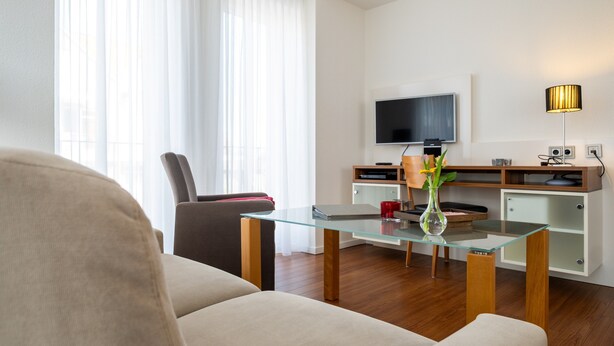 Un salon moderne avec une table basse en verre, un canapé, un téléviseur, une lampe et un meuble en bois.