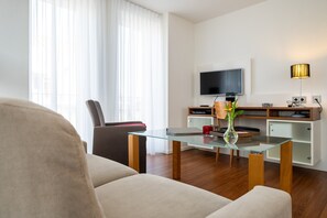 A modern living room with a glass coffee table, a sofa, a TV, a lamp, and a wooden cabinet. - 5-Star Comfort Holiday Home Jümmers – 'Marie', Prime Location by the Wadden Sea National Park (Wangerland-Horumersiel)
