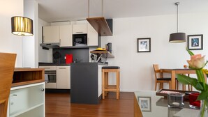 Une cuisine moderne avec des meubles blancs, un îlot central et un coin repas comprenant une table et des chaises en bois.
