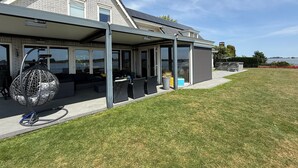 Een modern huis met een overdekt terras, grote ramen en uitzicht op het water.