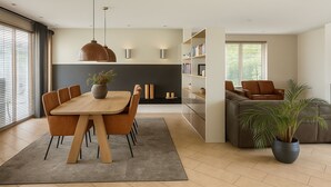 Een moderne woonkamer met een eethoek, een bank, een boekenkast en een groot raam met jaloezieën.
