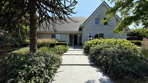 Een huis met een verharde oprit die naar een voordeur leidt, omgeven door goed onderhouden hagen en bomen.