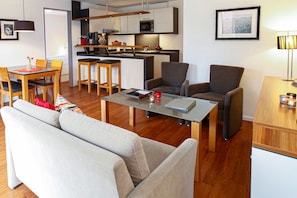 Ein modernes Wohnzimmer mit einer Couch, einem Couchtisch und einem Essbereich mit Stühlen, sowie einer kleinen Küche im Hintergrund.