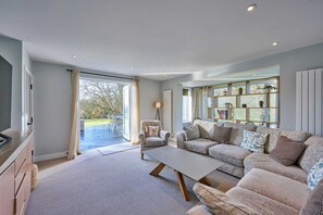 A spacious living room with a large sofa, a coffee table, and a dining area visible through an open door. - Host & Stay | Roundwood House (Taverham)
