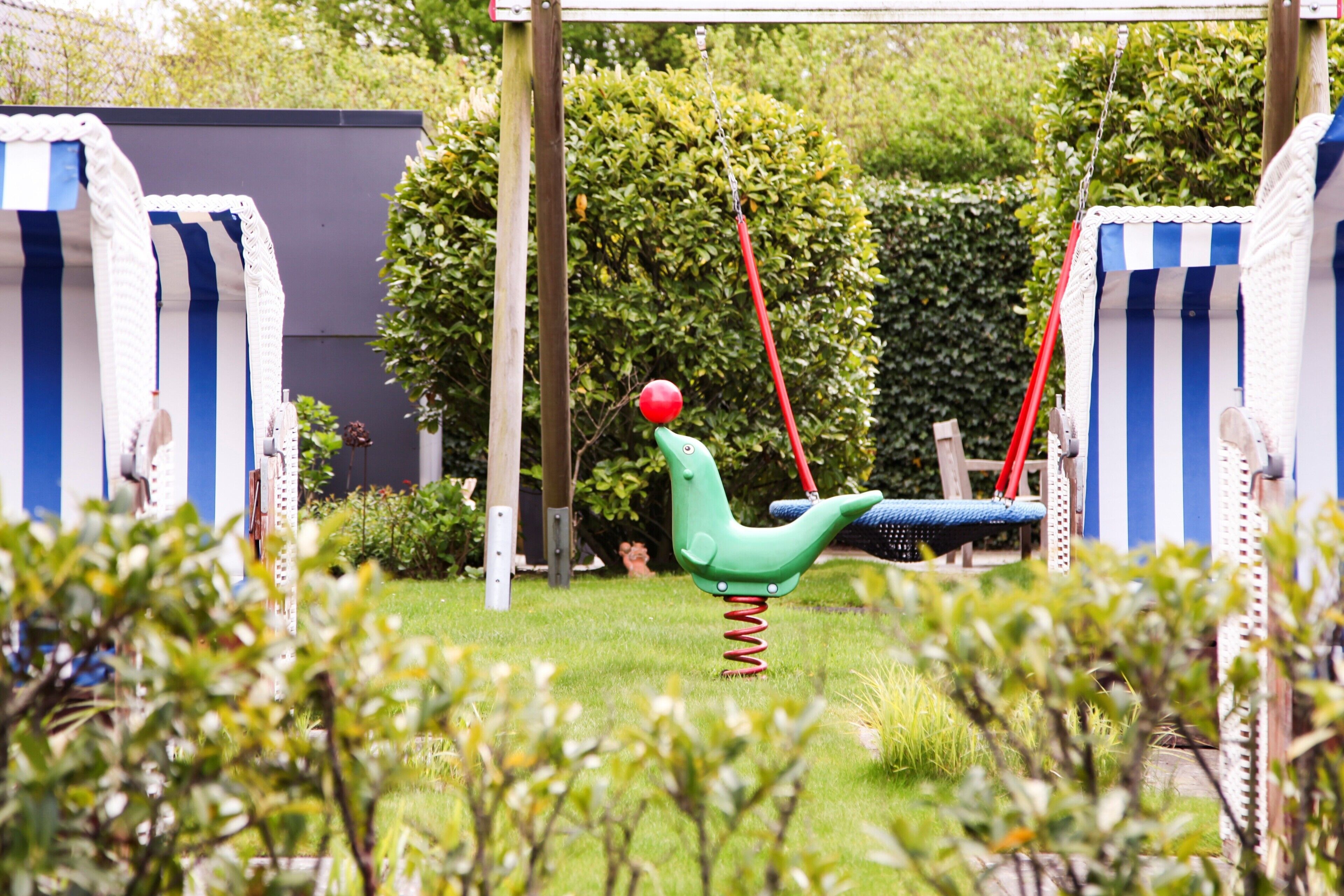 A swing set in a garden with striped fabric walls and a hedge in the background.