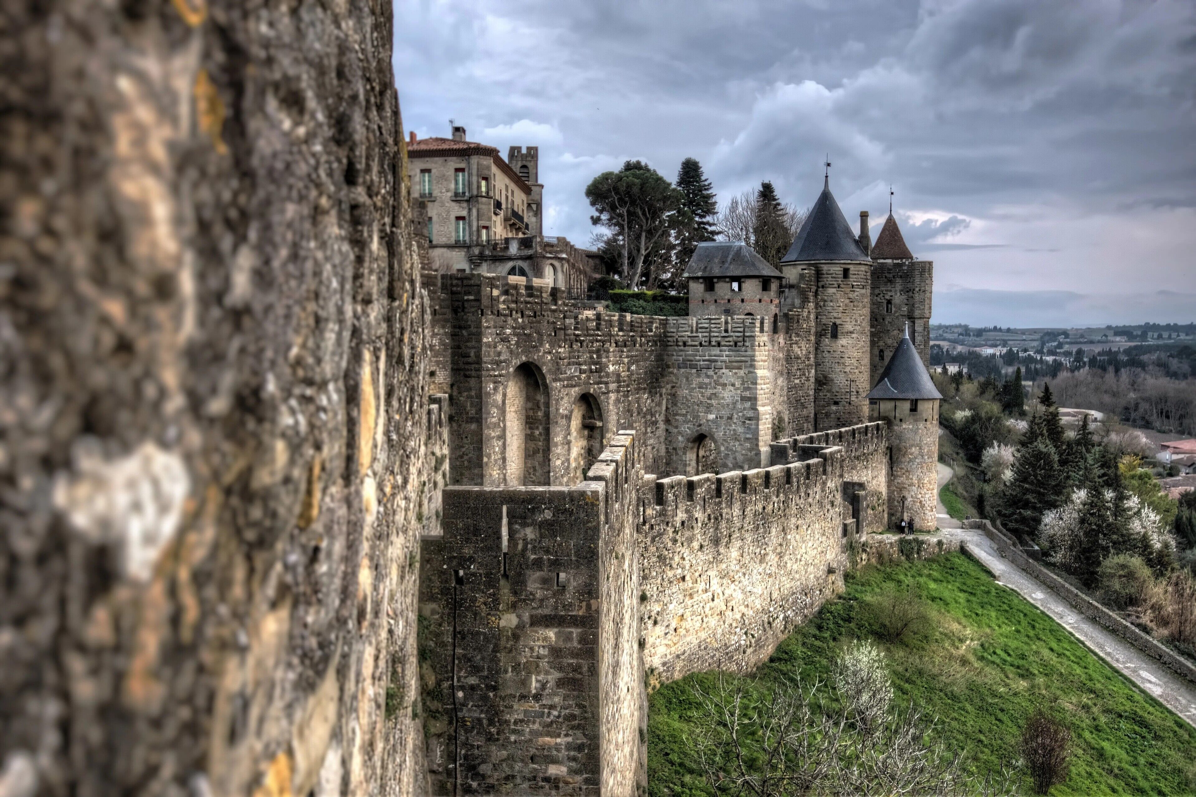 Eine historische Burg aus Stein mit mehreren Türmen, einer befestigten Mauer und einem Weg zum Eingang.