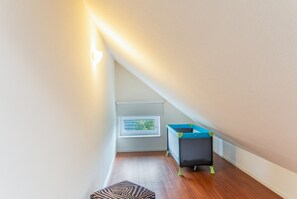 A small attic room with a window, a playpen, and a zebra-patterned ottoman. - 5-Star Comfort Holiday Home Jümmers - 'Niklas', Prime Location by the Wadden Sea National Park (Wangerland-Horumersiel)