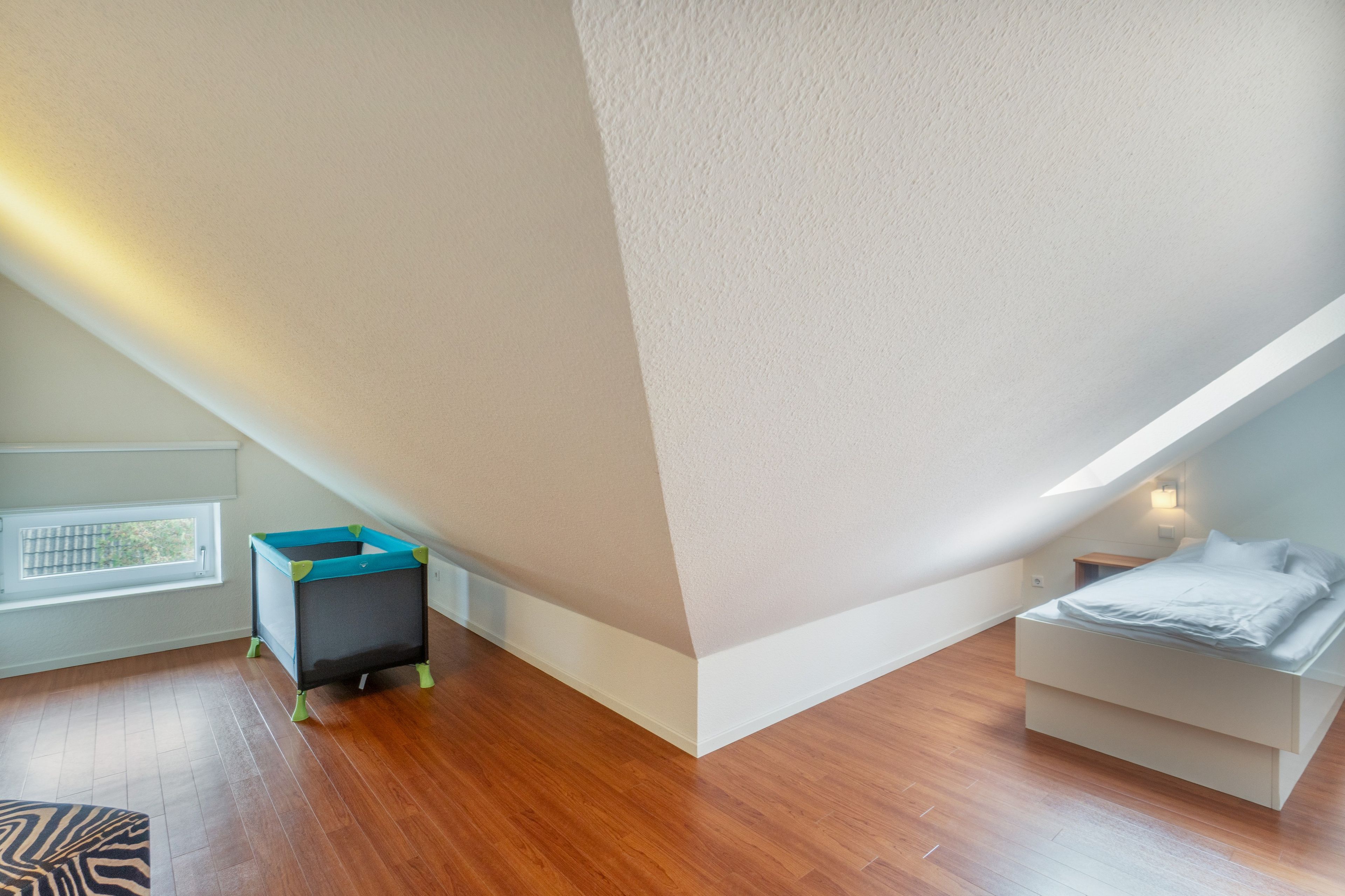 Une pièce avec un plafond en pente, un lit, une petite table et une fenêtre.
