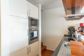 A compact kitchen with a built-in oven, microwave, and a kettle on the countertop. - 5-Star Comfort Holiday Home Jümmers - 'Niklas', Prime Location by the Wadden Sea National Park (Wangerland-Horumersiel)