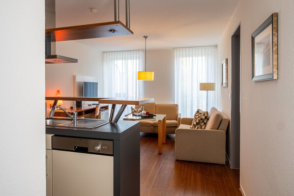 A modern kitchen with a dishwasher, a dining area with a table and chairs, a sofa, and a lamp.