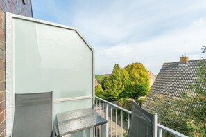 A balcony with a metal railing, a glass door, and a view of a tree and buildings in the background. - 5-Star Comfort Holiday Home Jümmers - 'Niklas', Prime Location by the Wadden Sea National Park (Wangerland-Horumersiel)