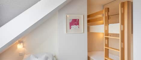 Ein Schlafzimmer mit Etagenbett, einem Einzelbett, einem gerahmten Bild an der Wand und einer geneigten Decke.