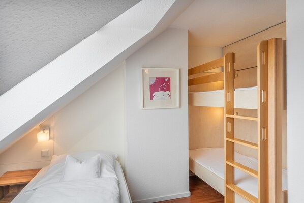 A bedroom with a bunk bed, a single bed, a framed picture on the wall, and a sloped ceiling. - 5-Star Comfort Holiday Home Jümmers - 'Niklas', Prime Location by the Wadden Sea National Park (Wangerland-Horumersiel)