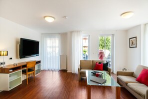 Un salon moderne avec un téléviseur à écran plat, des meubles en bois, une table basse en verre et un canapé agrémenté de coussins rouges.