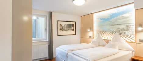 A hotel room with a double bed, a framed picture on the wall, a window, and a radiator.
